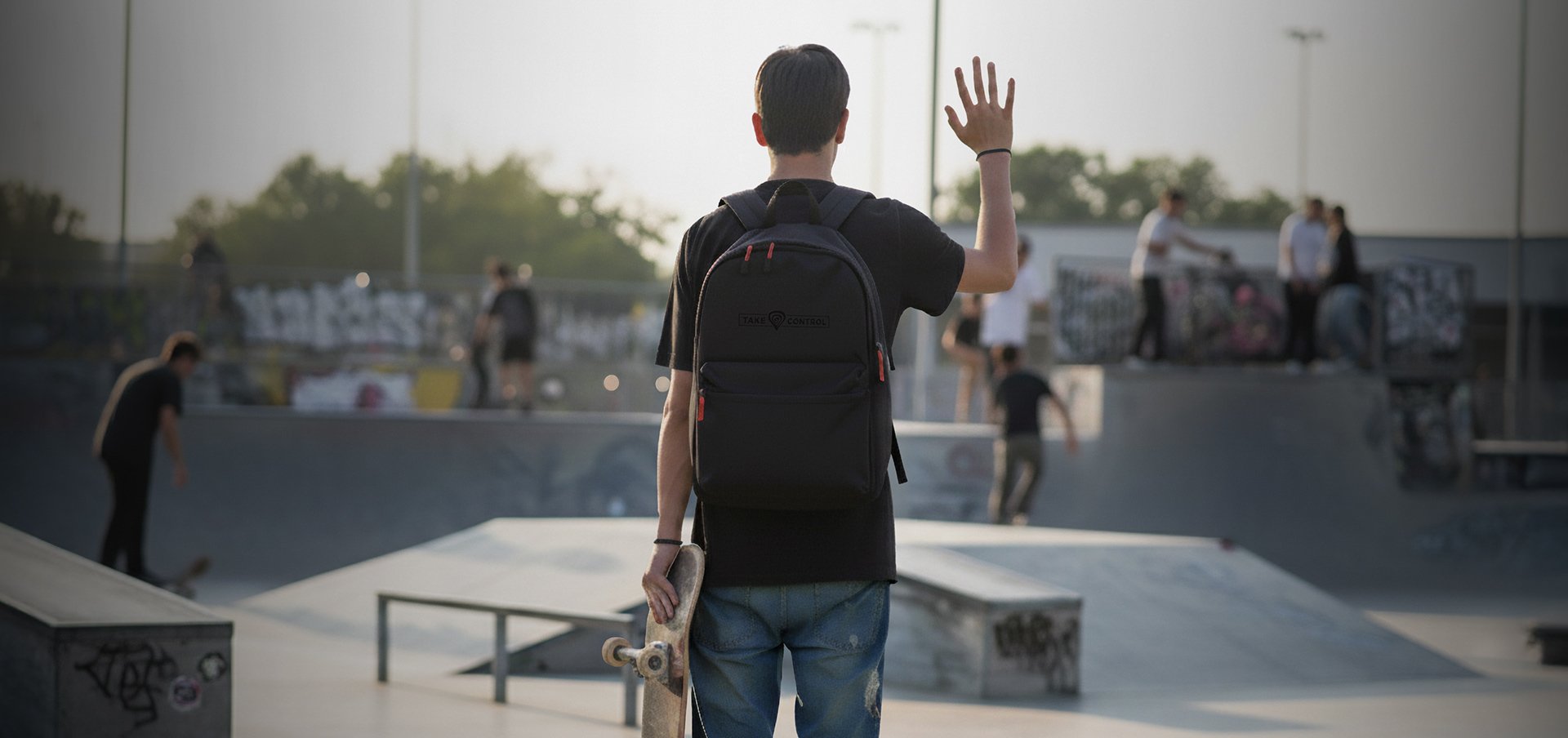 Osoba stojąca w skateparku, trzymająca deskorolkę i nosząca czarny plecak Genesis Pallad 200