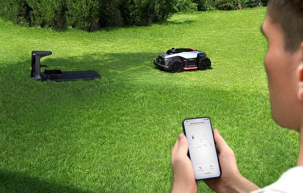 Mężczyzna steruje robotem koszącym za pomocą aplikacji w smartfonie