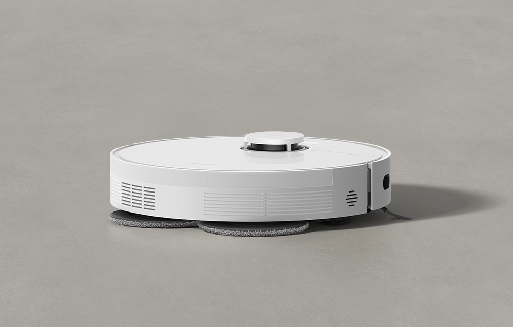 Biały robot sprząający z padami mopującymi na szarej podłodze.