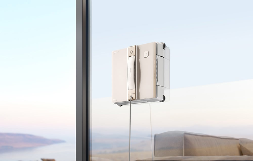 Robot do mycia okien przyklejony do dużego okna w salonie z widokiem na krajobraz