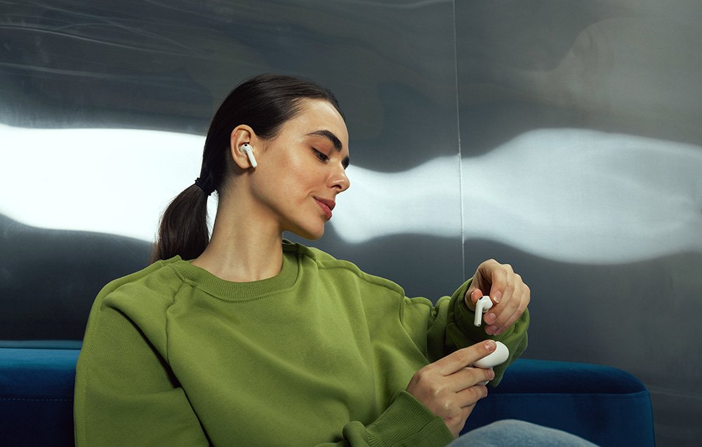 Kobieta w zielonej bluzie wyjmuje słuchawkę Edifier W260NC z etui, drugą słuchawkę ma już w uszach.