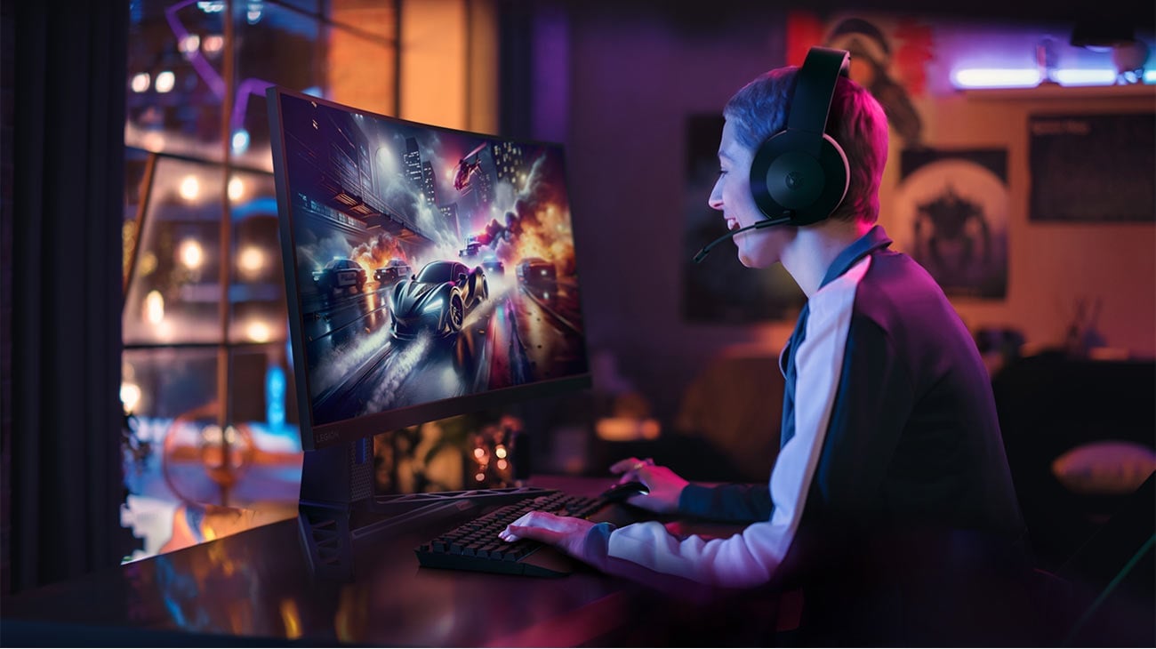 Monitor Lenovo R27qc-30 na biurku przed którym siedzi młoda osoba ze słuchawkami na głowie i gra w grę komputerową