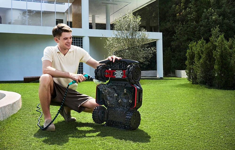Mężczyzna czyści robota koszącego wodą z ogrodowego węża.