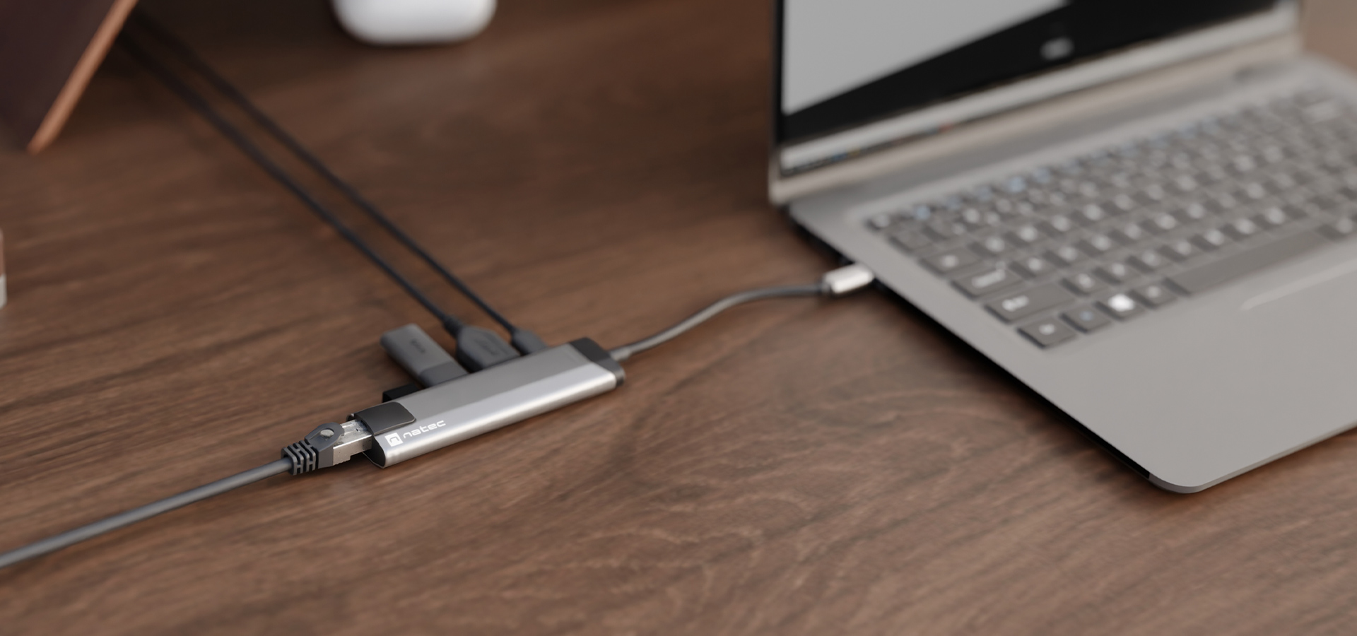 Adapter wieloportowy podłączony do laptopa na drewnianym biurku z wieloma widocznymi portami