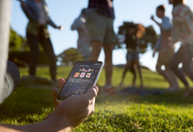 Osoba korzystająca z telefonu Xperia E4 z aplikacją Party Share; w tle tańczą inne osoby