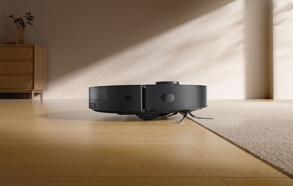 Robot sprzątający Dreame D20 w czarnym kolorze pokazany z boku, stoi na drewnianej podłodze obok dywanu