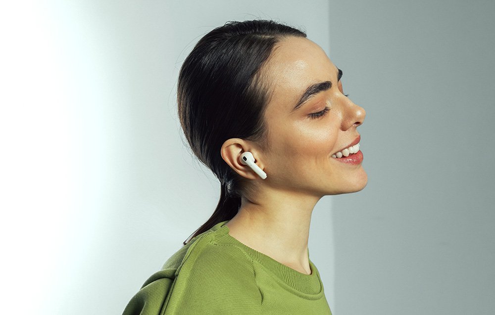 Uśmiechnięta kobieta słucha muzyki przy użyciu słuchawek Edifier W260NC.