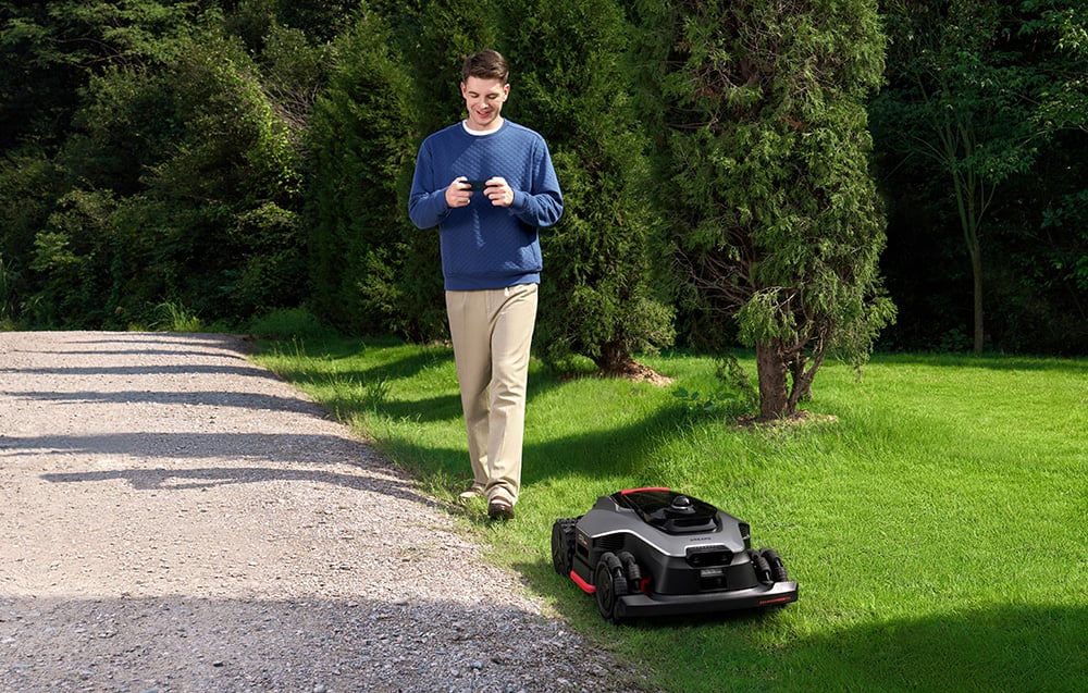 Mężczyzna idzie obok robota koszącego poruszającego się po trawniku