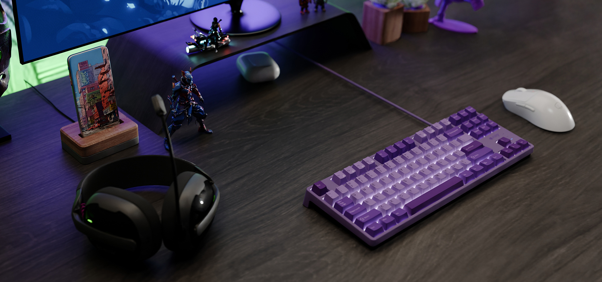 Fioletowa klawiatura i biała myszka na ciemnym drewnianym biurku z słuchawkami i figurkami.
