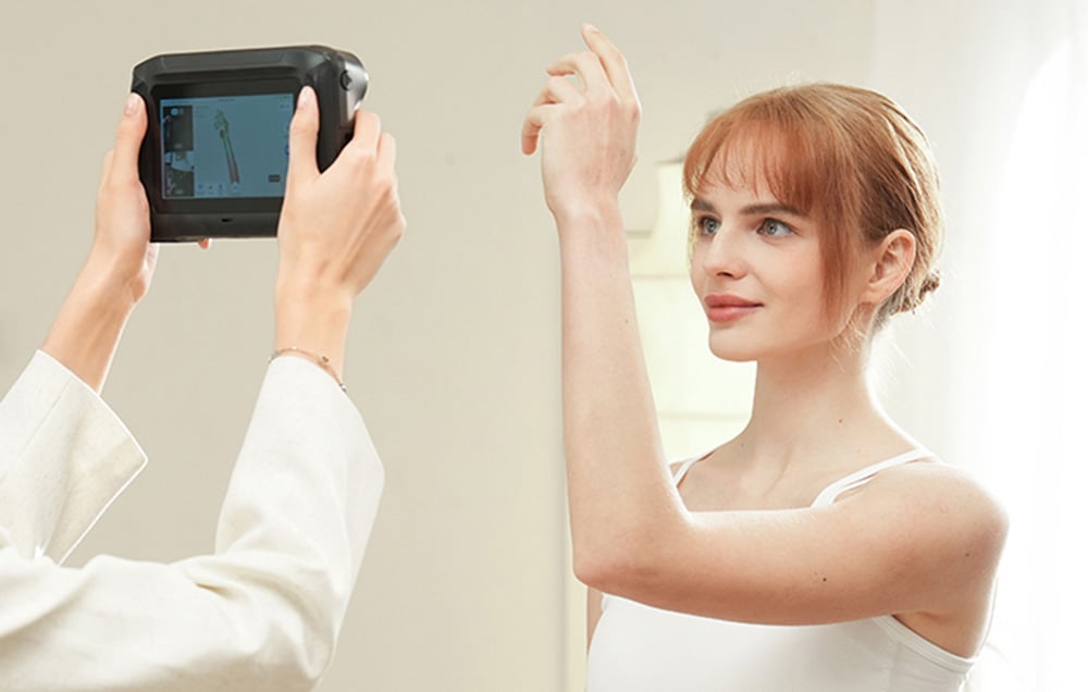 Osoba skanuje ręcznym skanerem 3D ramię kobiety stojącej z uniesioną ręką