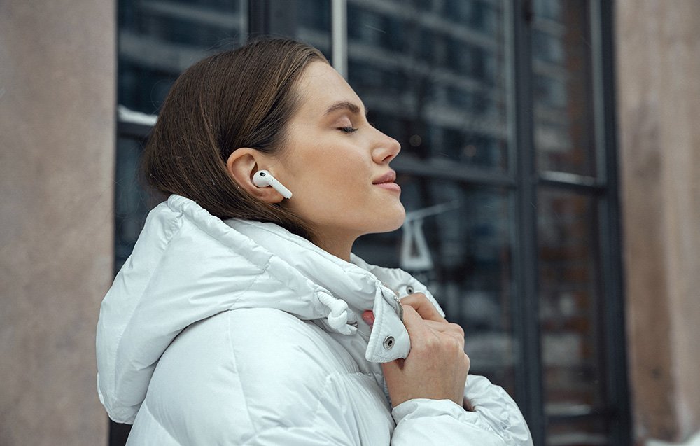Kobieta w białej kurtce słucha muzyki – w uszach ma słuchawki TWS Edifier W260NC.
