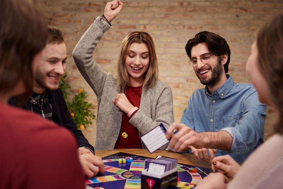 Opaskę SmartBand 2 można spersonalizować jednym z czterech pasków Grupa znajomych gra w grę planszową. Dziewczyna ma na nadgarstku różową opaskę SmartBand 2