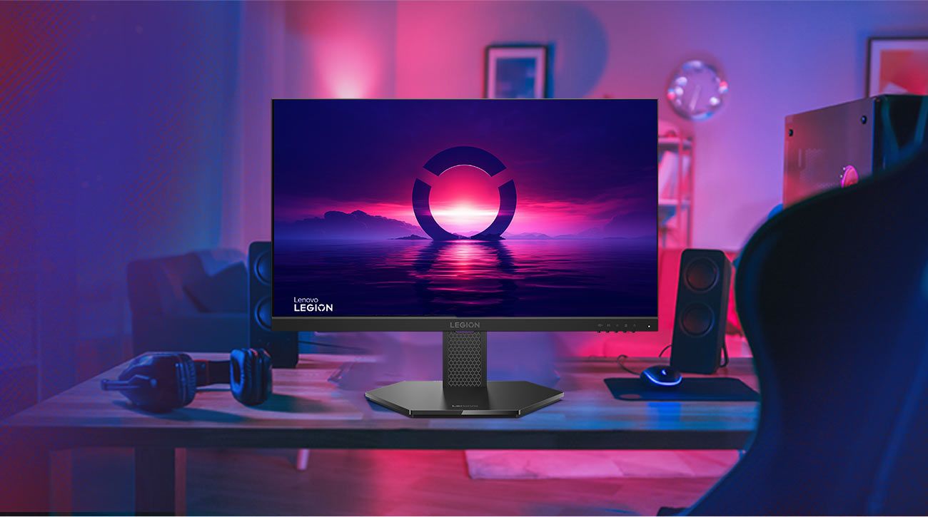 Monitor Lenovo Legion 24-10 z kolorową tapetą na ekranie stojący na biurku, obok głośniki, klawiatura i słuchawki