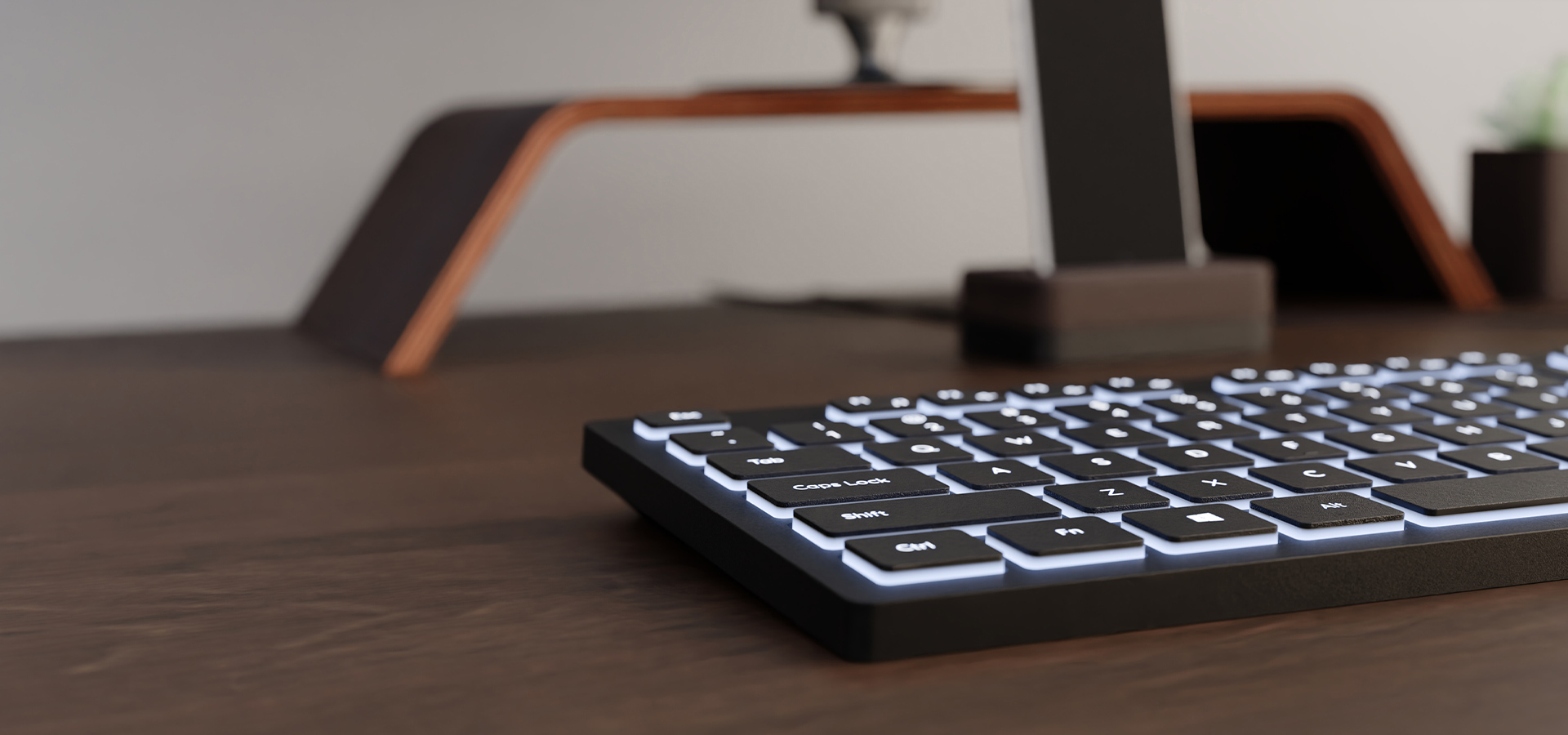 Klawiatura z białym podświetleniem na drewnianym biurku i podstawą monitora w tle