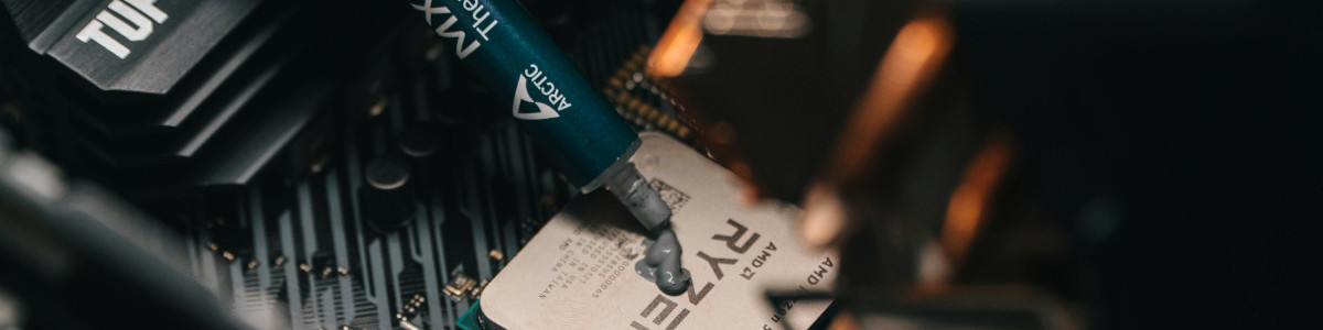 zbliżenie na procesor AMD osadzony w sockecie płyty głównej, widoczna strzykawka z pastą termoprzewodzącą w trakcie wyciskania