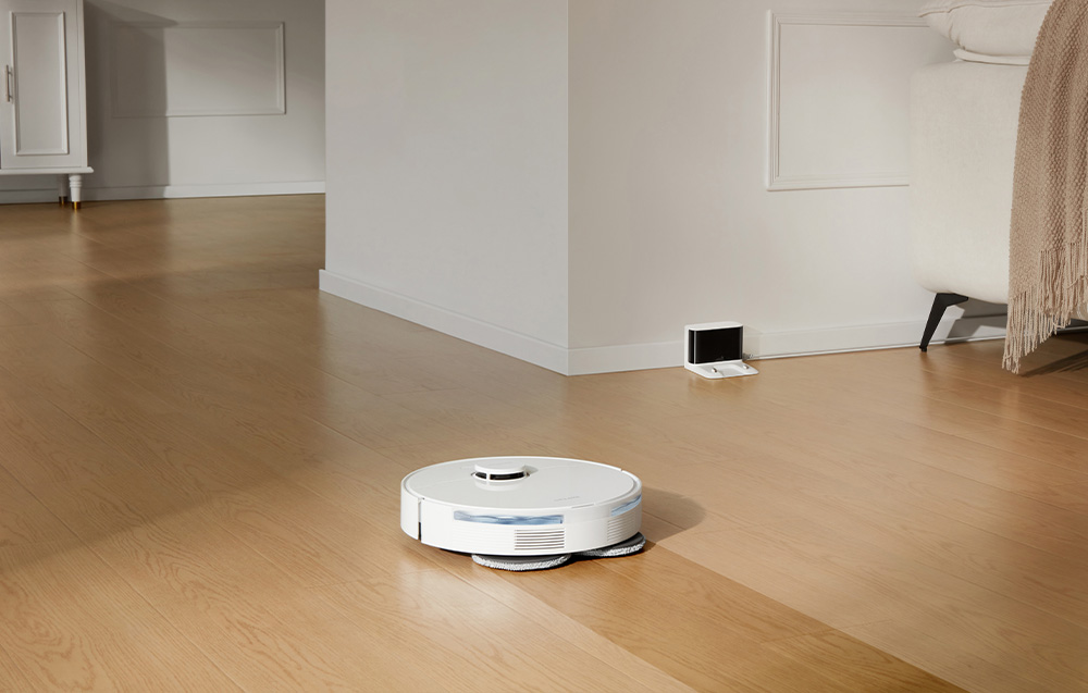 Robot sprzątający mopuje podłogę. Po prawej stronie stacja dokująca przy ścianie.