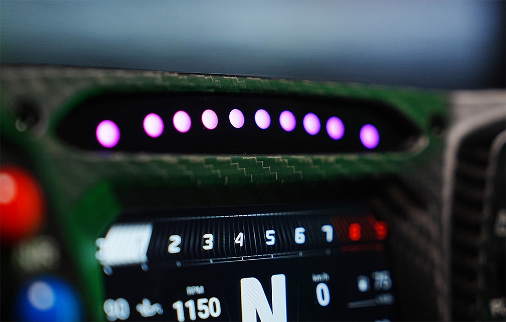 Zbliżenie na podświetlenie LED u góry kierownicy MOZA Racing Lamborghini Essenza SCV12 RS070, świecące na różowo i fioletowo.