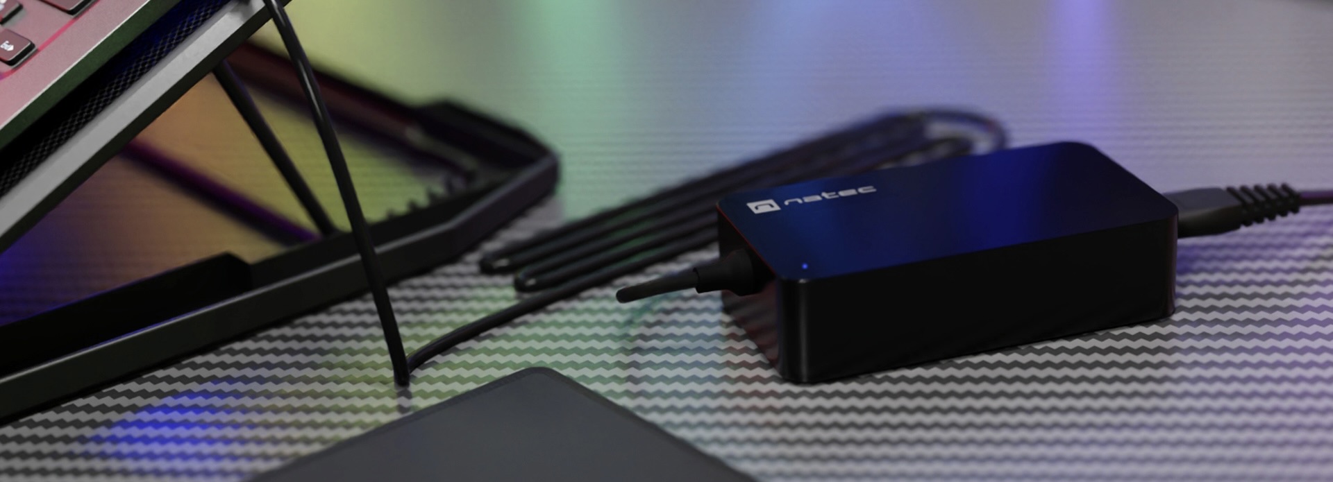 Ładowarka Natec Grayling 65W USB-C do laptopów, tabletów i telefonów, umieszczona na teksturowanej powierzchni z kablami w pobliżu